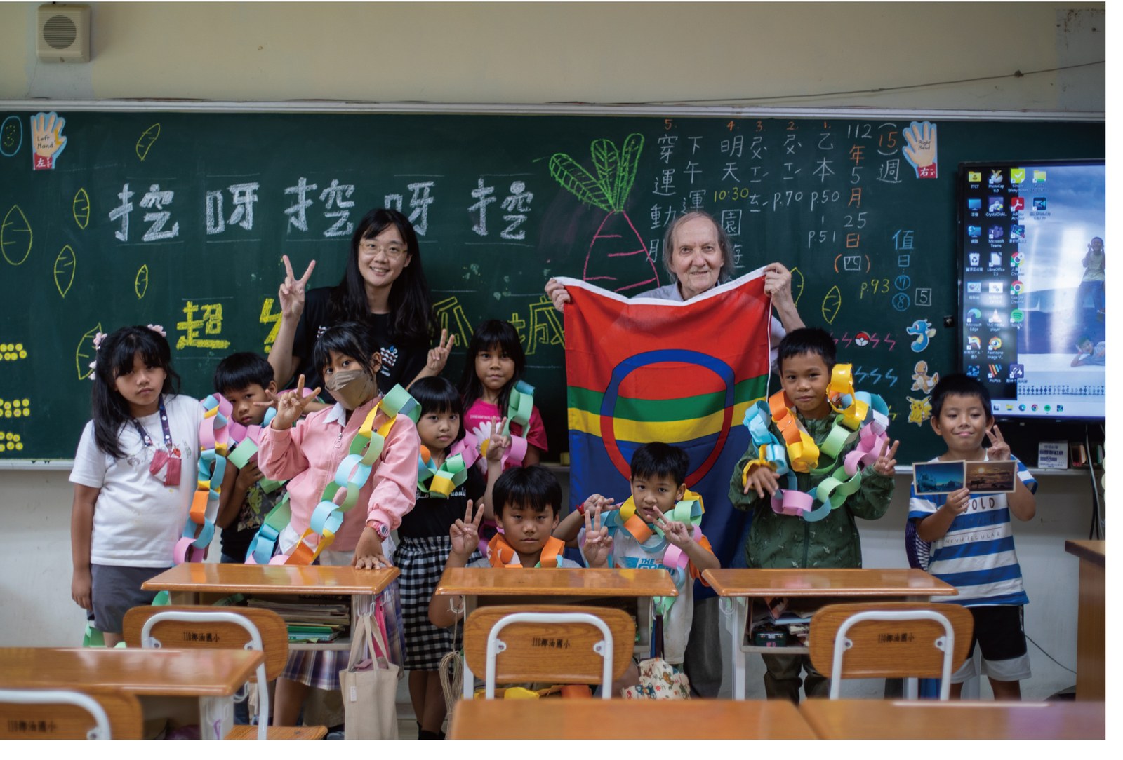 Sámi artist Hans Ragnar Mathisen holding the Sámi flag with Taiwanese schoolchildren
